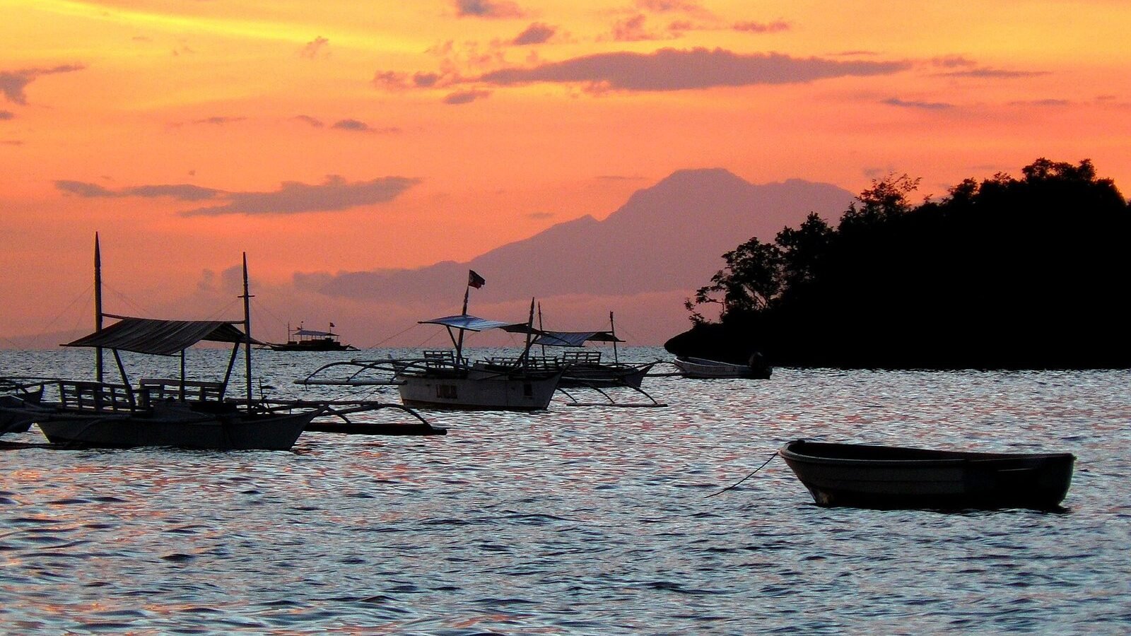 Outrigger boats silhouetted against an orange sunset at Alona Beach, Panglao Island, Bohol, Philippines
