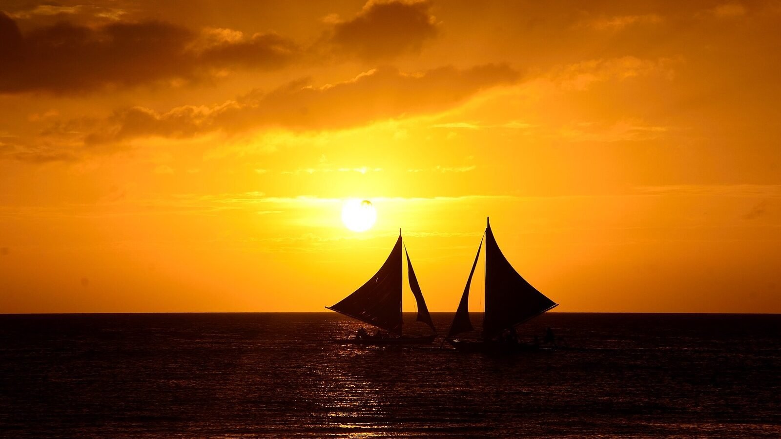 Paraw sailboats silhouetted against a golden sunset off White Beach, Boracay, Philippines