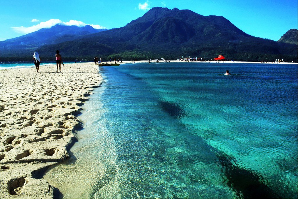 A white sandbar and turquoise shallows with the volcanic peaks of Camiguin Island behind, Philippines