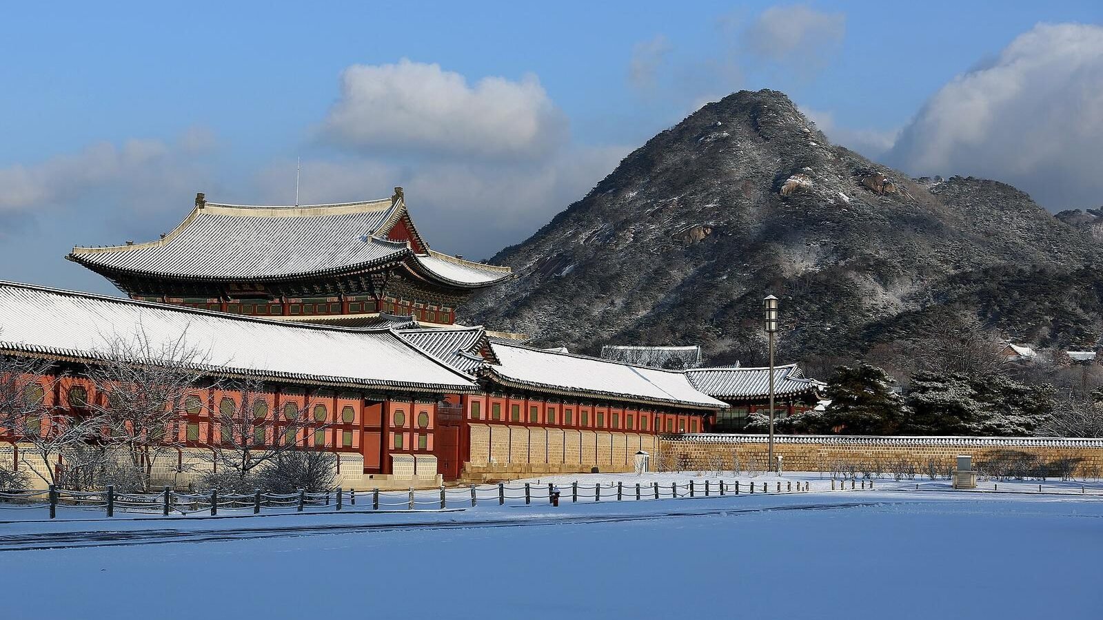 Snow covering the roofs of Gyeongbokgung Palace with mountains behind in Seoul, South Korea