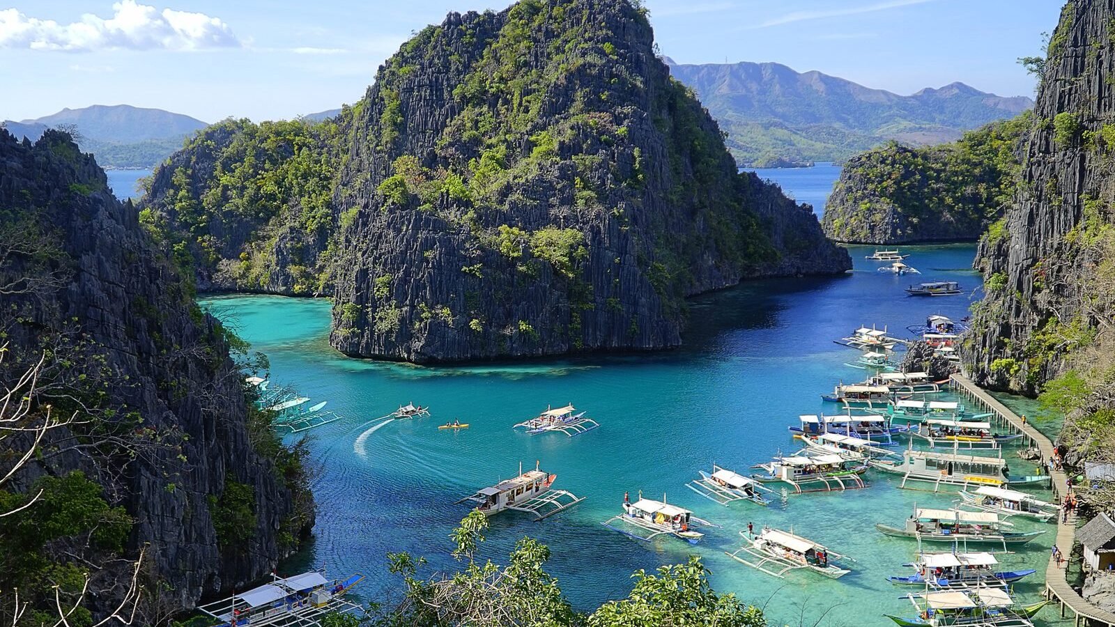 Outrigger boats moored below the limestone cliffs at Kayangan Lake, Coron, Palawan, Philippines