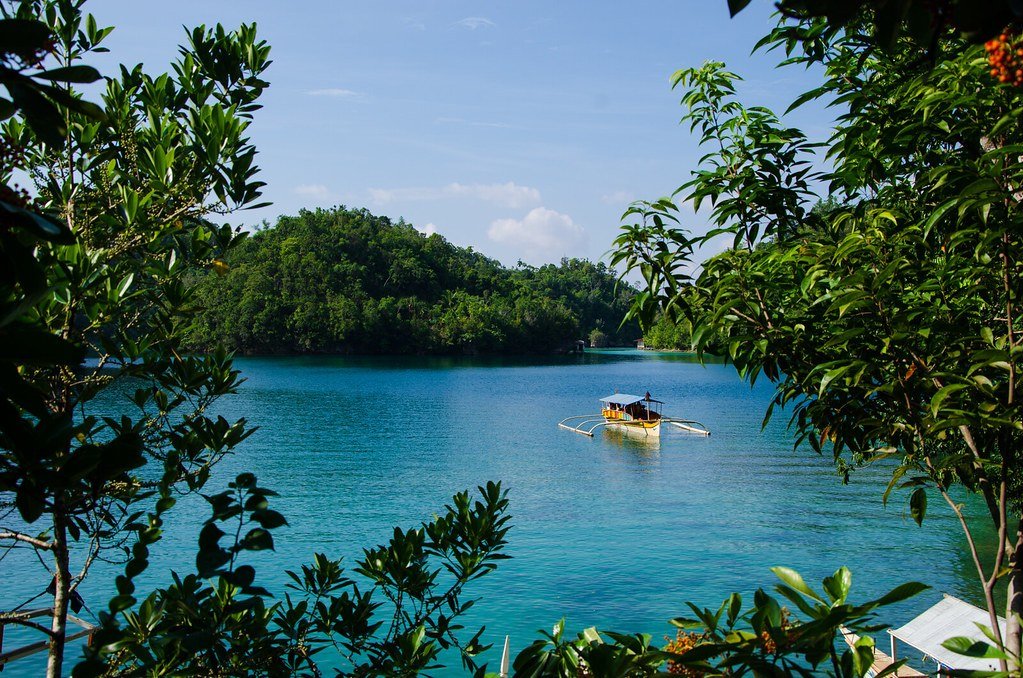 A boat on the turquoise water of Sohoton Cove framed by jungle on Bucas Grande Island, Surigao del Norte, Philippines