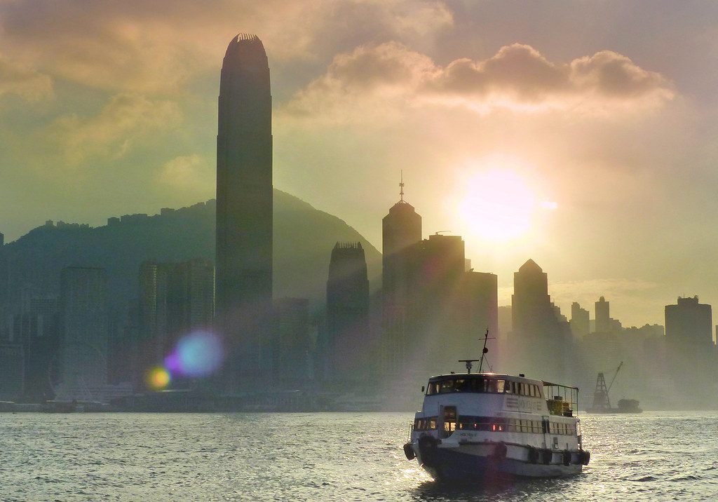 Hong Kong Island skyline and Victoria Harbour at sunset with a ferry crossing the water