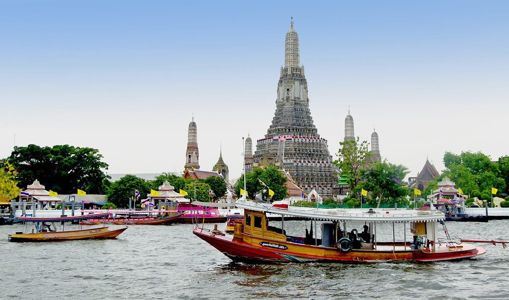 Wat Arun temple on the Chao Phraya river with longtail boats in Bangkok, Thailand